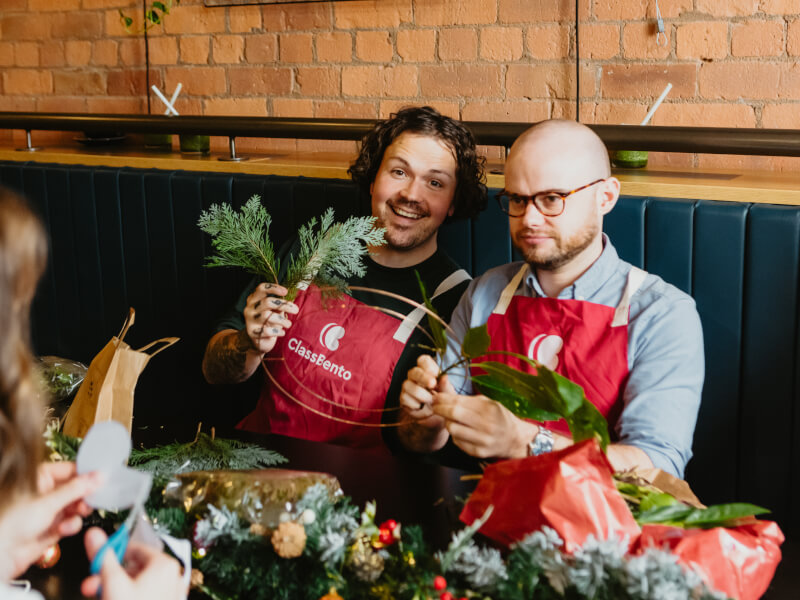 Smiling men in aprons making Christmas wreaths